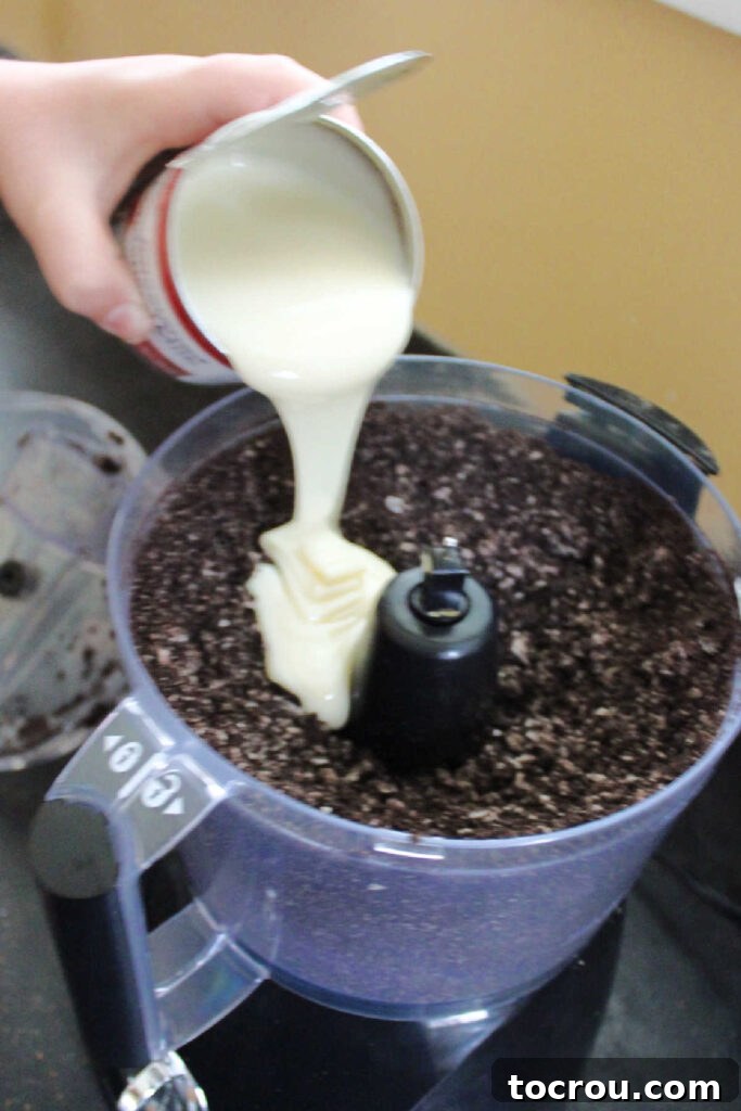 Creamy No-Bake Oreo Truffles 3 Pouring can of condensed milk into food processor filled with Oreo crumbs.