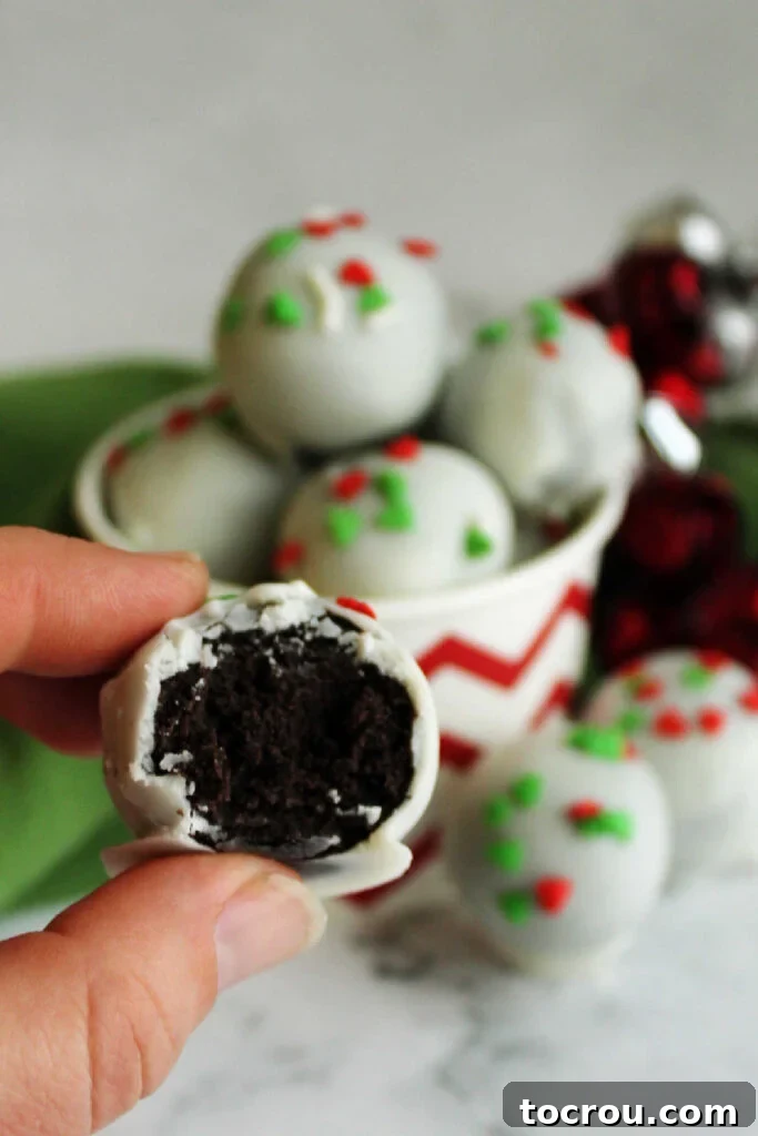 Creamy No-Bake Oreo Truffles 10 Hand holding an Oreo ball that was made with condensed milk showing the rich chocolate inside and the white chocolate shell.