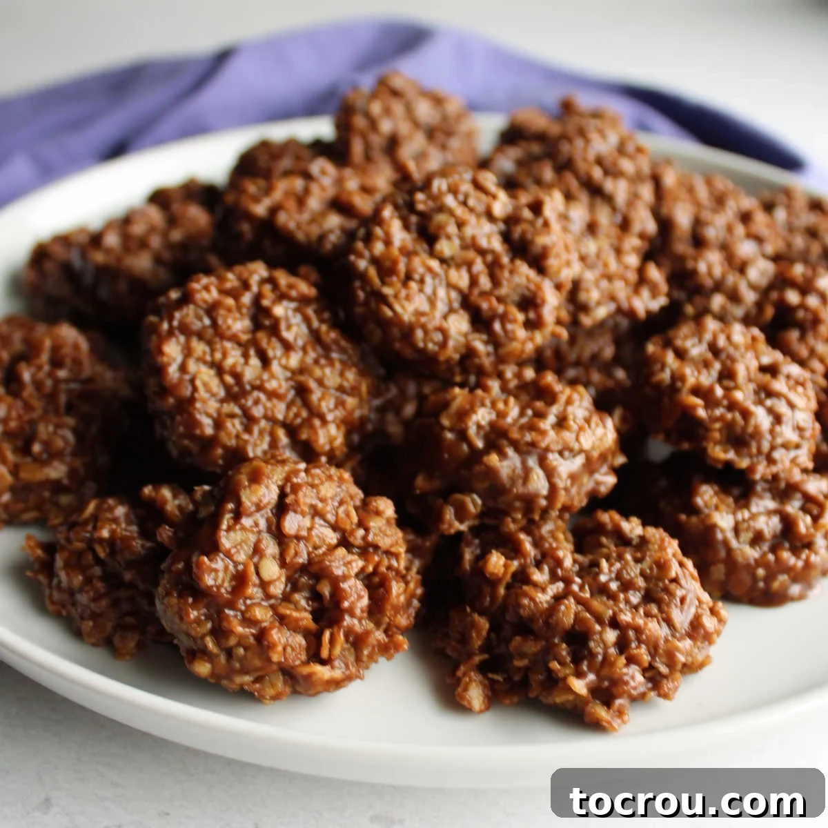 Sink your teeth into a chocolate and peanut butter loaded no bake cookie and you'll instantly know why they're a classic. This recipe comes together quickly and doesn't require you to turn on the oven. Plate of shiny chocolate no bake peanut butter and oatmeal cookies ready to be eaten.
