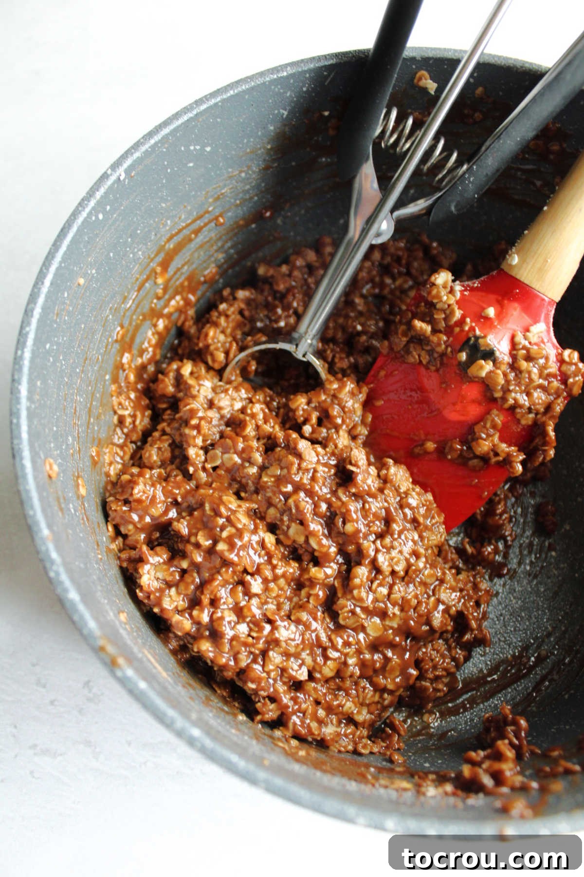 Chocolate Peanut Butter No-Bake Oatmeal Delights 3 sauce pan with cookie scoop and chocolate oatmeal mixture.
