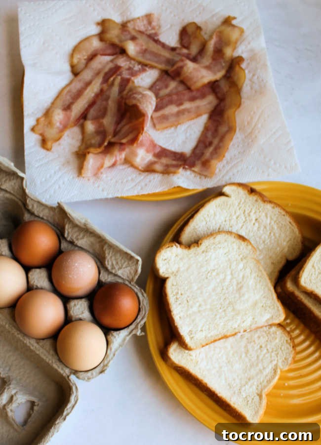 Ingredients Ready for Sheet Pan Eggs in a Basket Slices of bread with holes cut out, fresh eggs, and partially cooked bacon laid out on a sheet pan, ready for assembly.