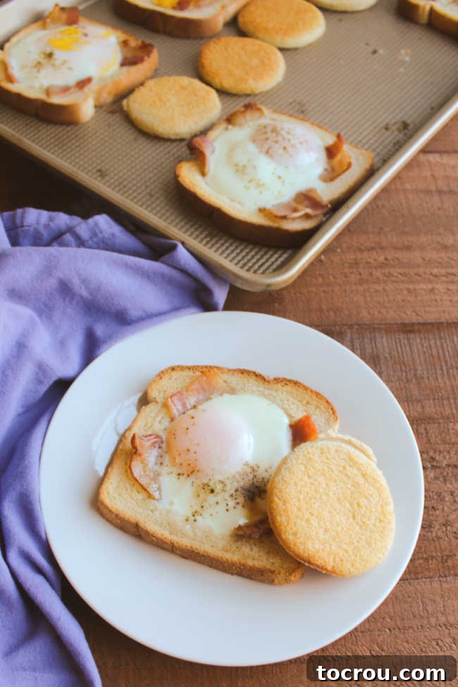 Individual Serving of Sheet Pan Egg in a Basket A single serving of bacon and egg in a basket on a plate, complete with the toasted bread cutout, with the remaining sheet pan in the background.