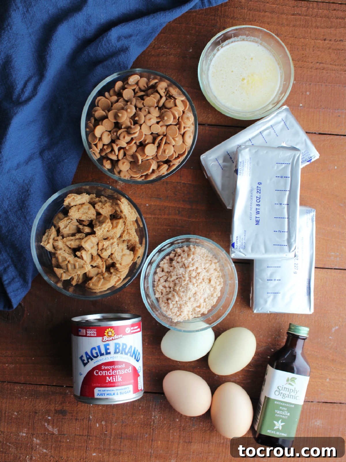 Key Ingredients for Peanut Butter Toffee Cheesecake Ingredients including cream cheese, sweetened condensed milk, peanut butter chips, peanut butter cookies, toffee bits, eggs, vanilla, and melted butter ready to be made into peanut butter cheesecake.