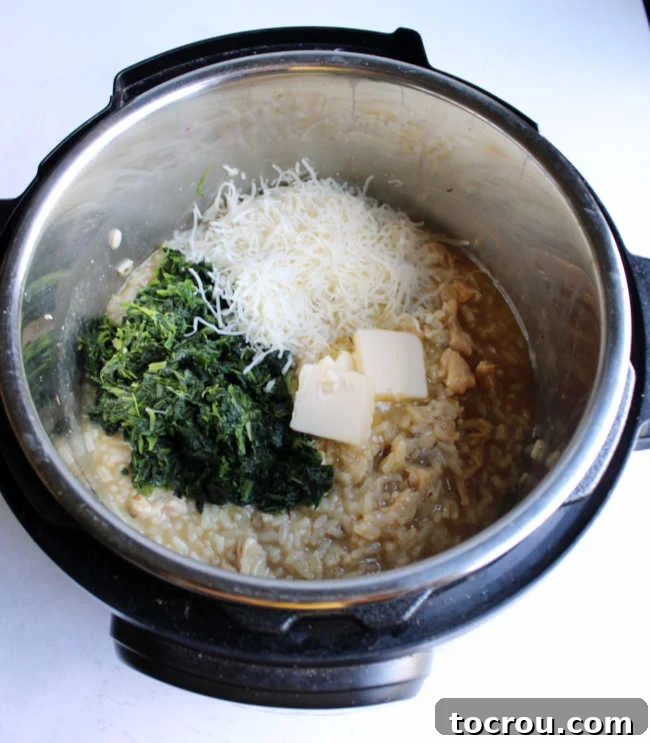 instant pot of freshly made risotto with shredded spinach, cheese and pats of butter on top ready to be stirred in.