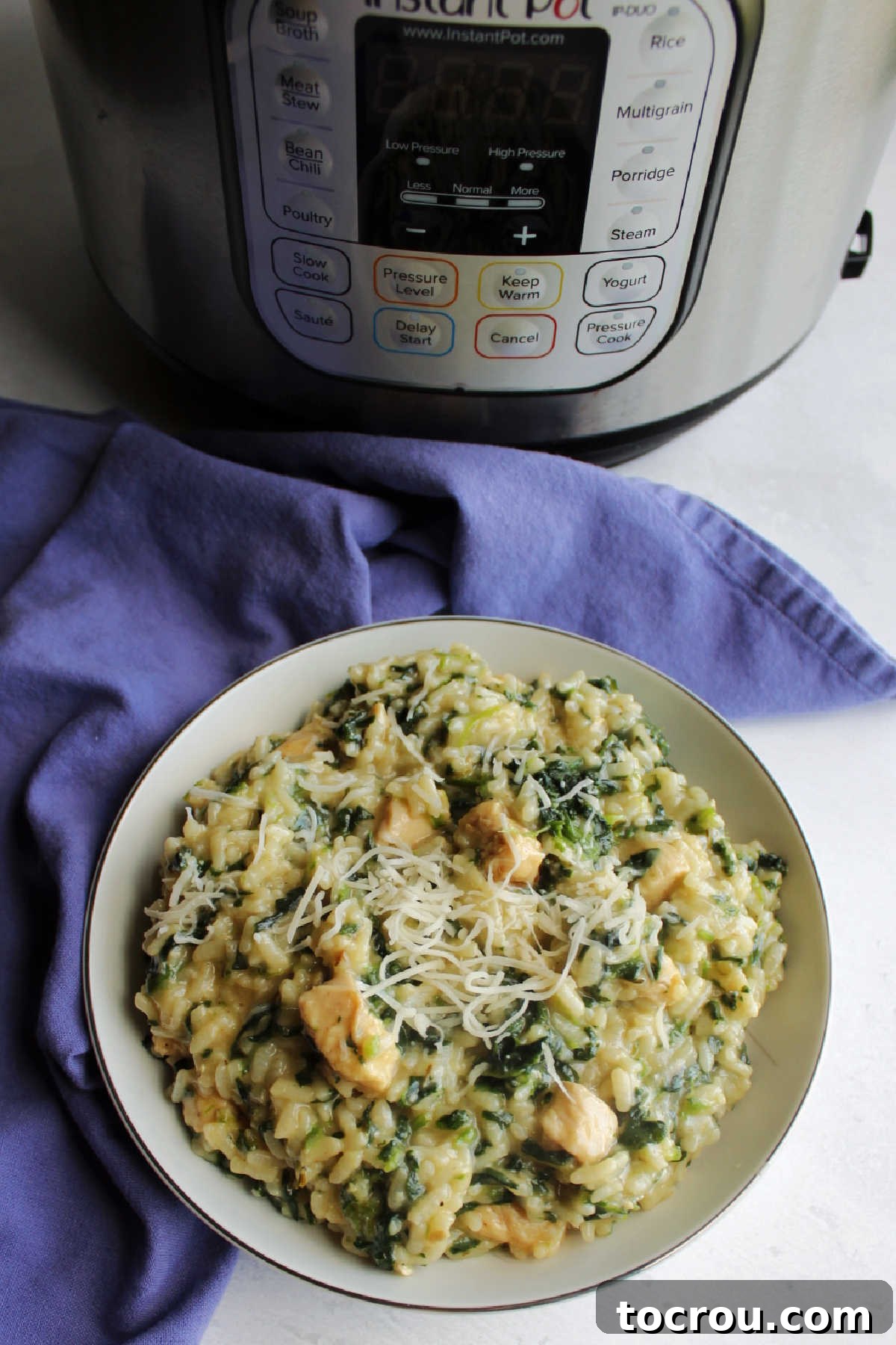 bowl of creamy spinach and chicken risotto topped with shredded Parmesan cheese on top in front of instant pot.