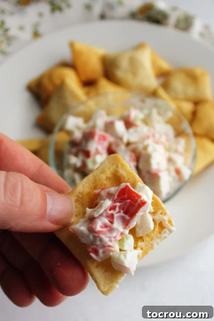 Kani Salad 3 Hand holding pita chip with pink and white crab salad on top.