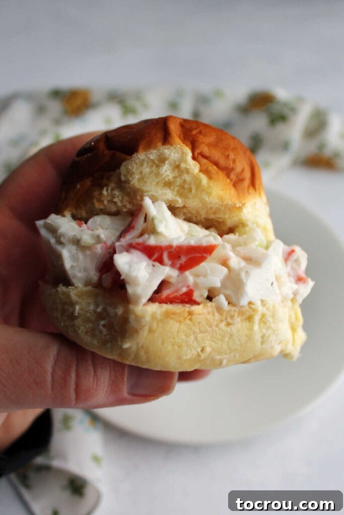 Kani Salad 5 Hand holding a crab salad sandwich with imitation crab salad on a Hawaiian roll.