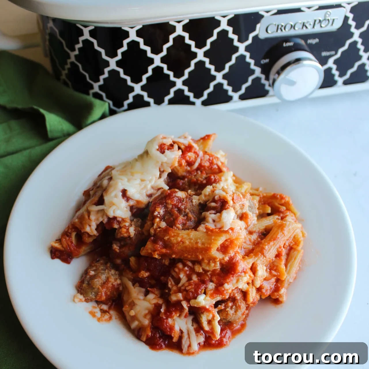 Serving of baked penne with cheese and sausage in front of a slow cooker.