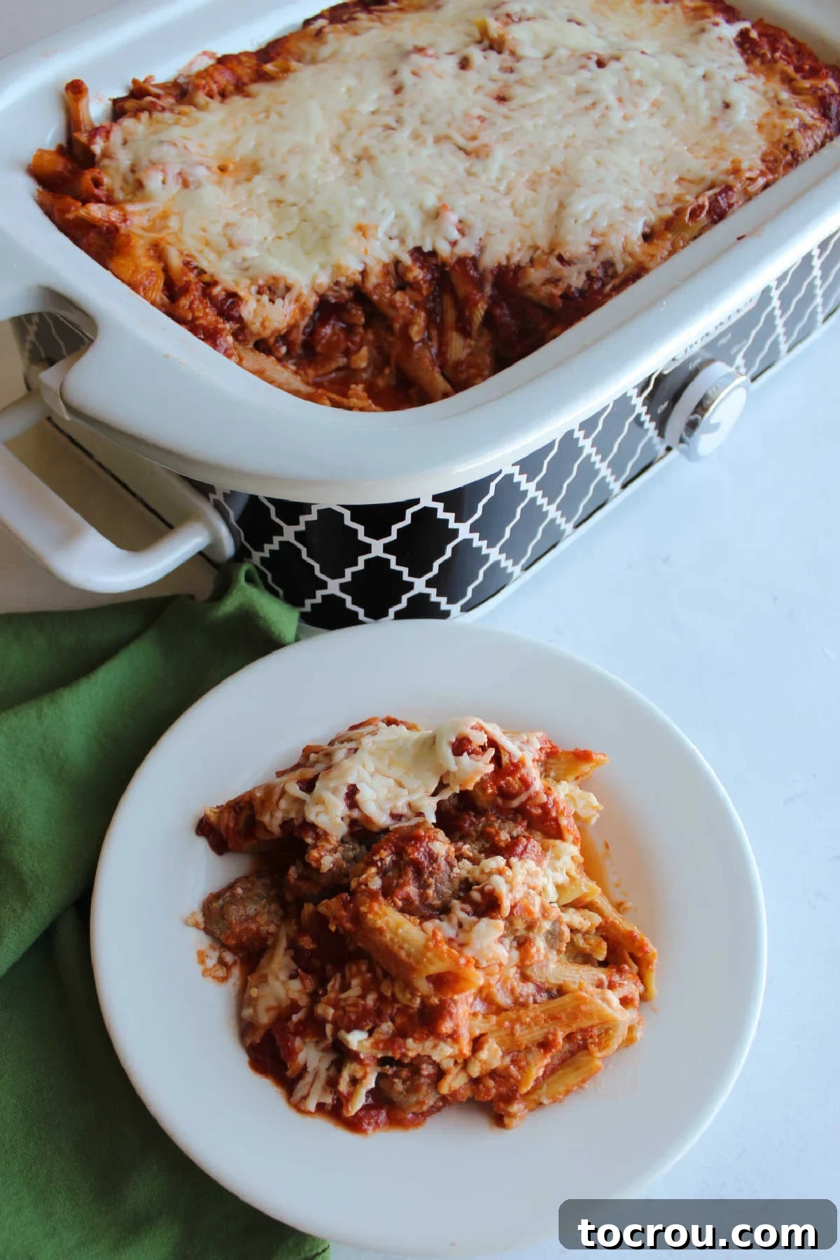 Baked penne with Italian sausage and cheese next to slow cooker filled with more baked pasta.