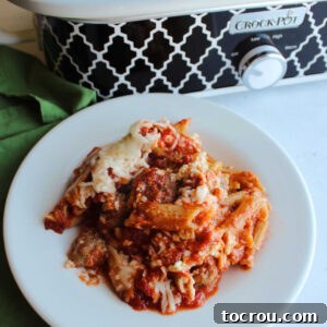 Serving of baked penne with cheese and sausage in front of crockpot.