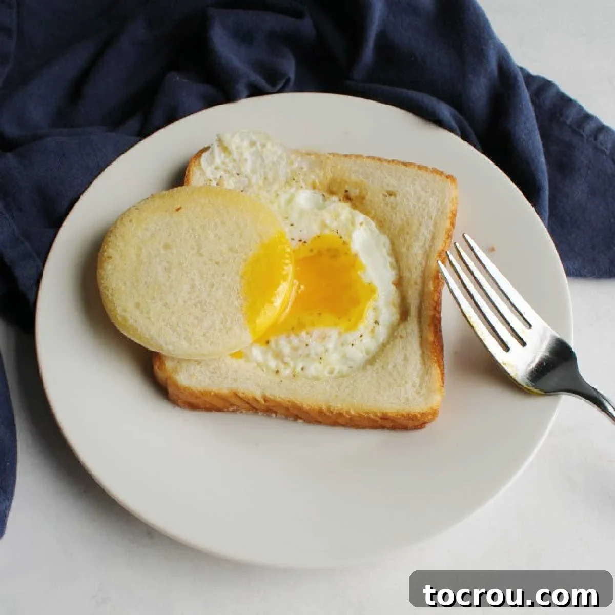 Egg in a hole on plate with bread circle dipped in runny yolk, ready to be enjoyed as a delicious breakfast.