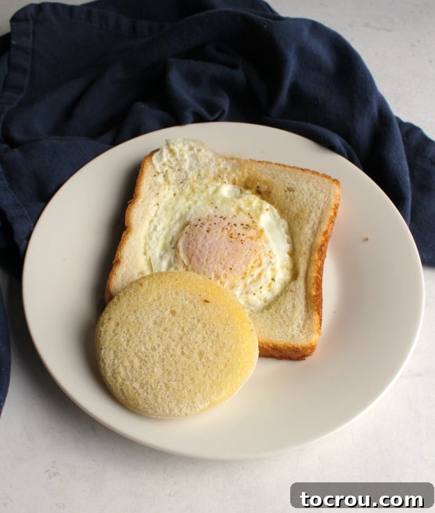 Egg in a bread basket on plate with circle of toast over top, ready to eat with a fork.