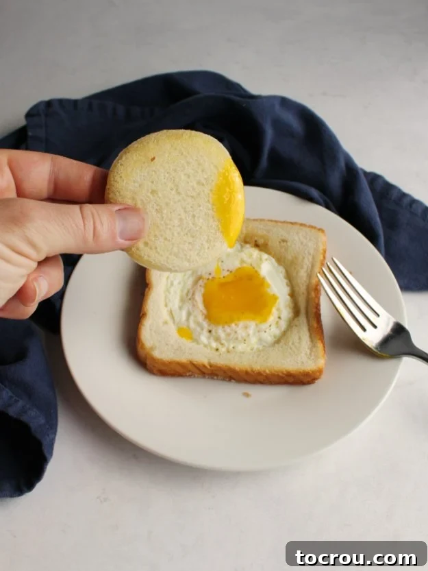 Close up of toast with an egg in the middle of it and runny yolk in the center, ready to be eaten.