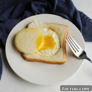 Egg in a hole on plate with bread circle dipped in runny yolk.