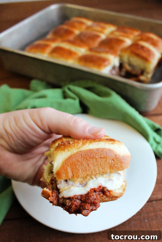 Pizza Burger Bites 5 Hand holding slider filled with saucy meat mixture, melted cheese and garlic butter on top.