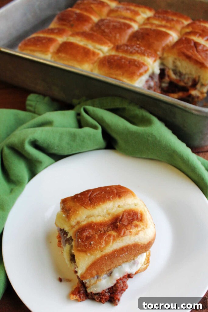 Pizza Burger Bites 6 Pizza burger slider on plate with pan of remaining sliders in background.