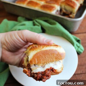 Hand holding pizza burger slider with melty cheese and garlic butter coated bun.