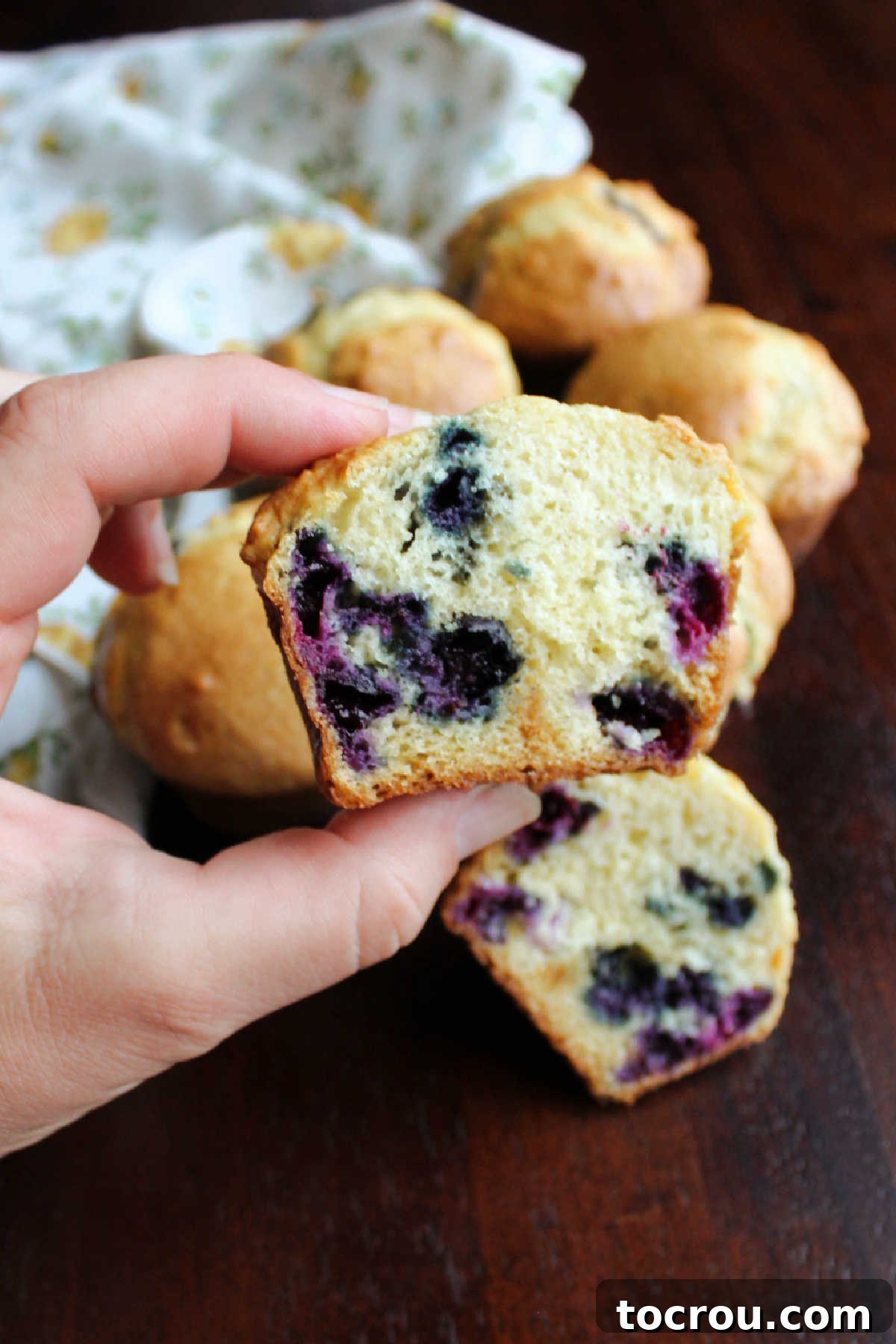 Hand Holding Blueberry Muffin Half Hand holding half of a soft blueberry muffin, revealing its tender interior and generous blueberries.