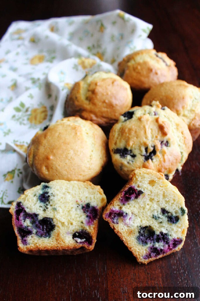 Freshly Baked Blueberry Muffins Pile of freshly baked muffins with one cut in half, showcasing berries and a soft interior.
