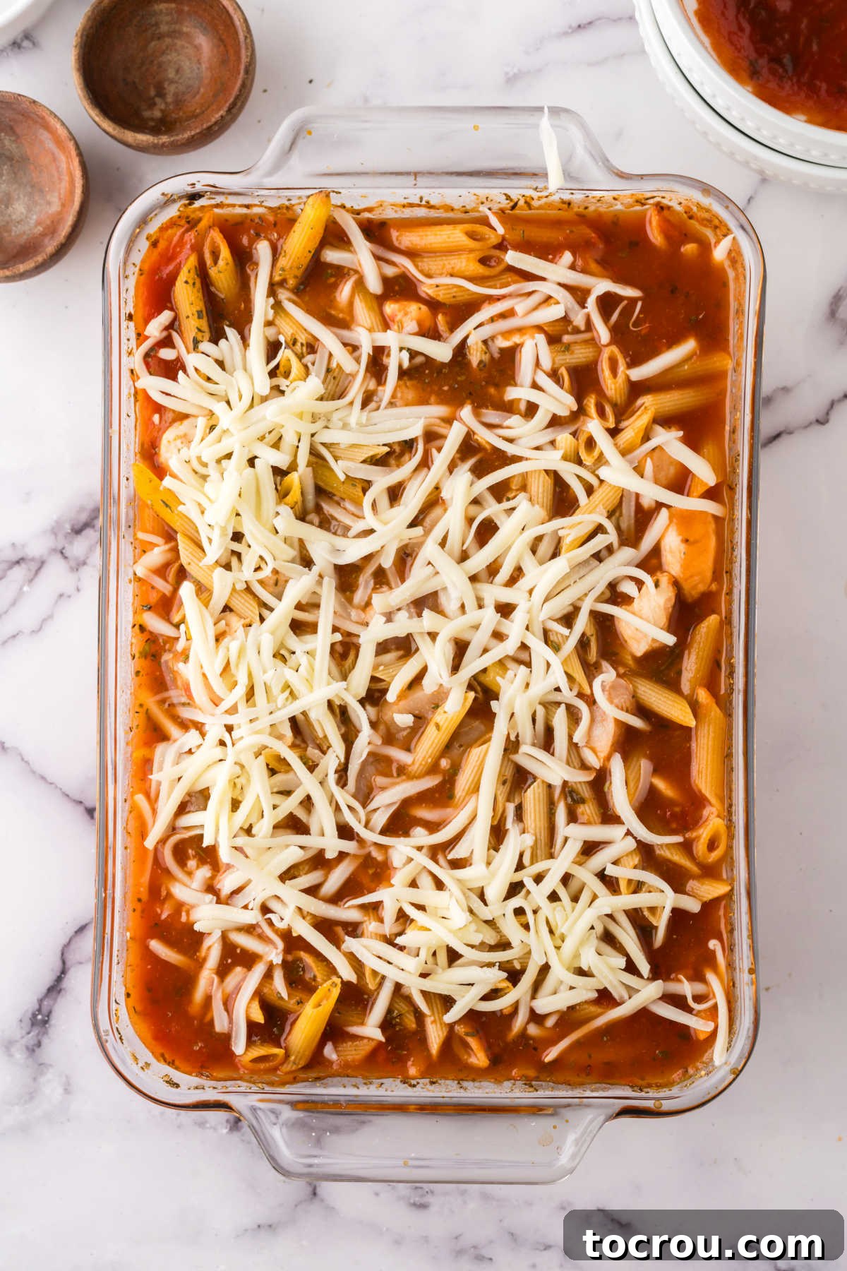 Dump-and-Bake Chicken Pasta Casserole 5 Adding shredded cheese to partially baked no boil chicken pasta bake, ready to go back in the oven.