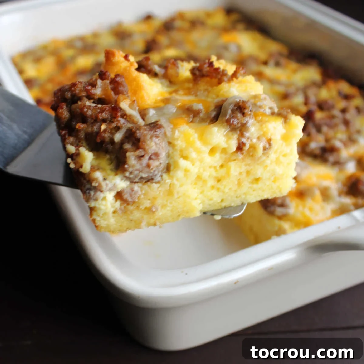 Savory Sausage Cornbread Morning Bake 2 Spatula lifting out piece of egg casserole with cornbread, sausage and cheddar cheese.