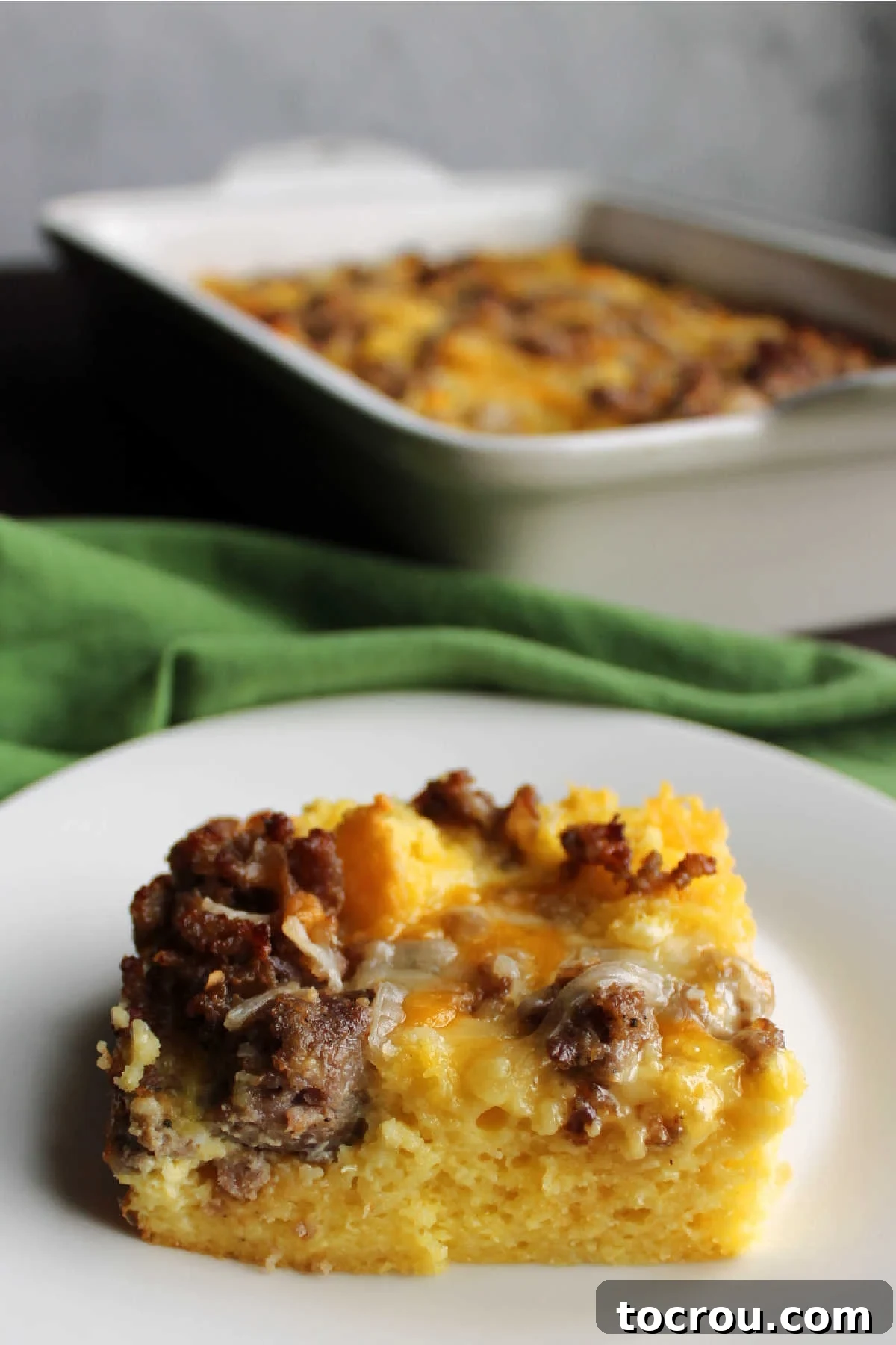 Savory Sausage Cornbread Morning Bake 6 Piece of sausage, cheese, egg and cornbread casserole served in front of baking dish.