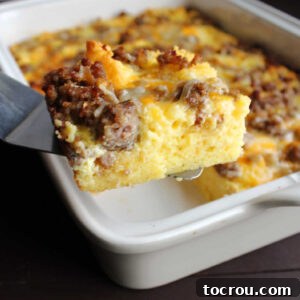 Spatula lifting out piece of egg casserole with cornbread, sausage and cheddar cheese.