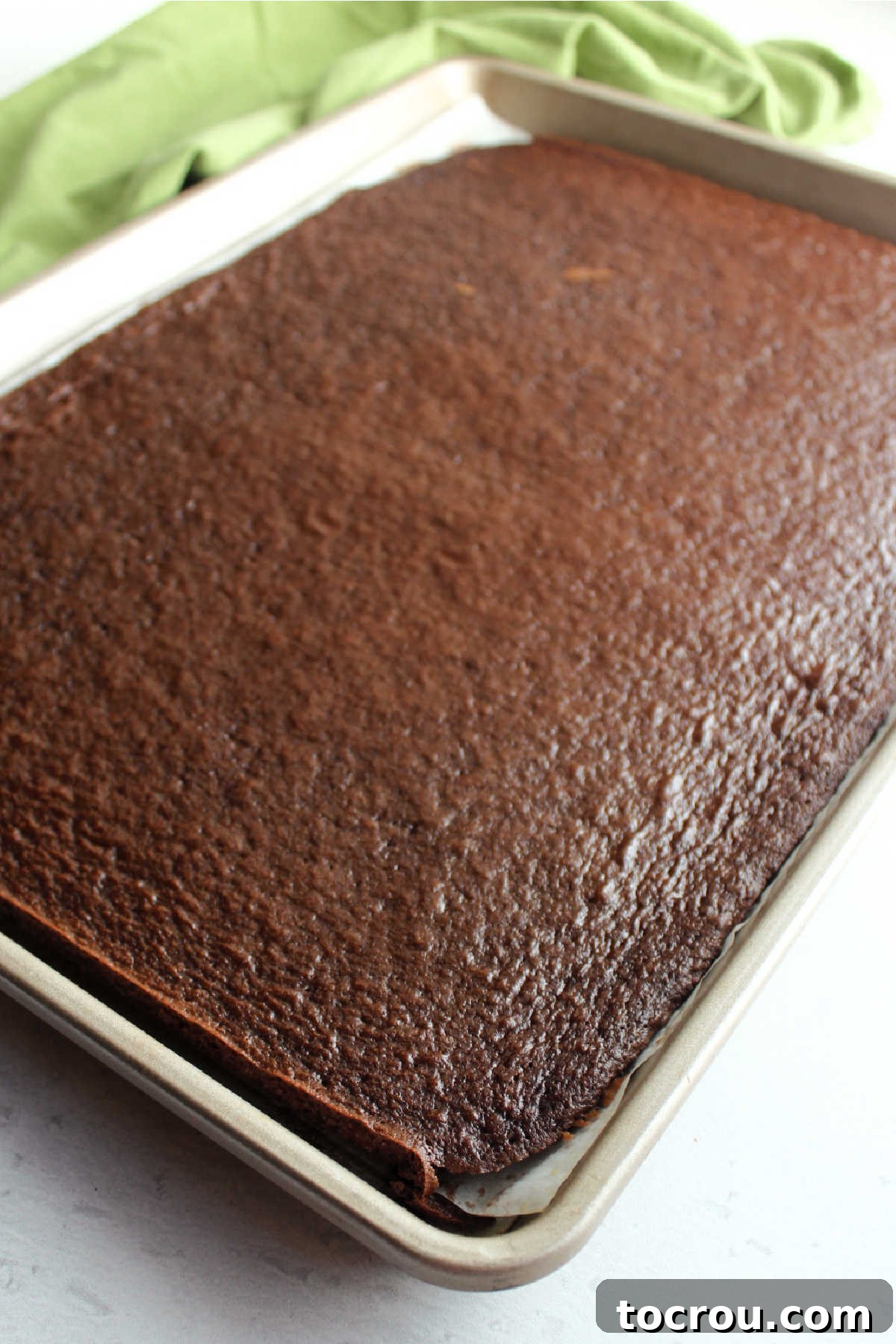 A sheet pan showcasing a perfectly baked, thin layer of chocolate cake, prepared and ready to be transformed into exquisite petit fours.