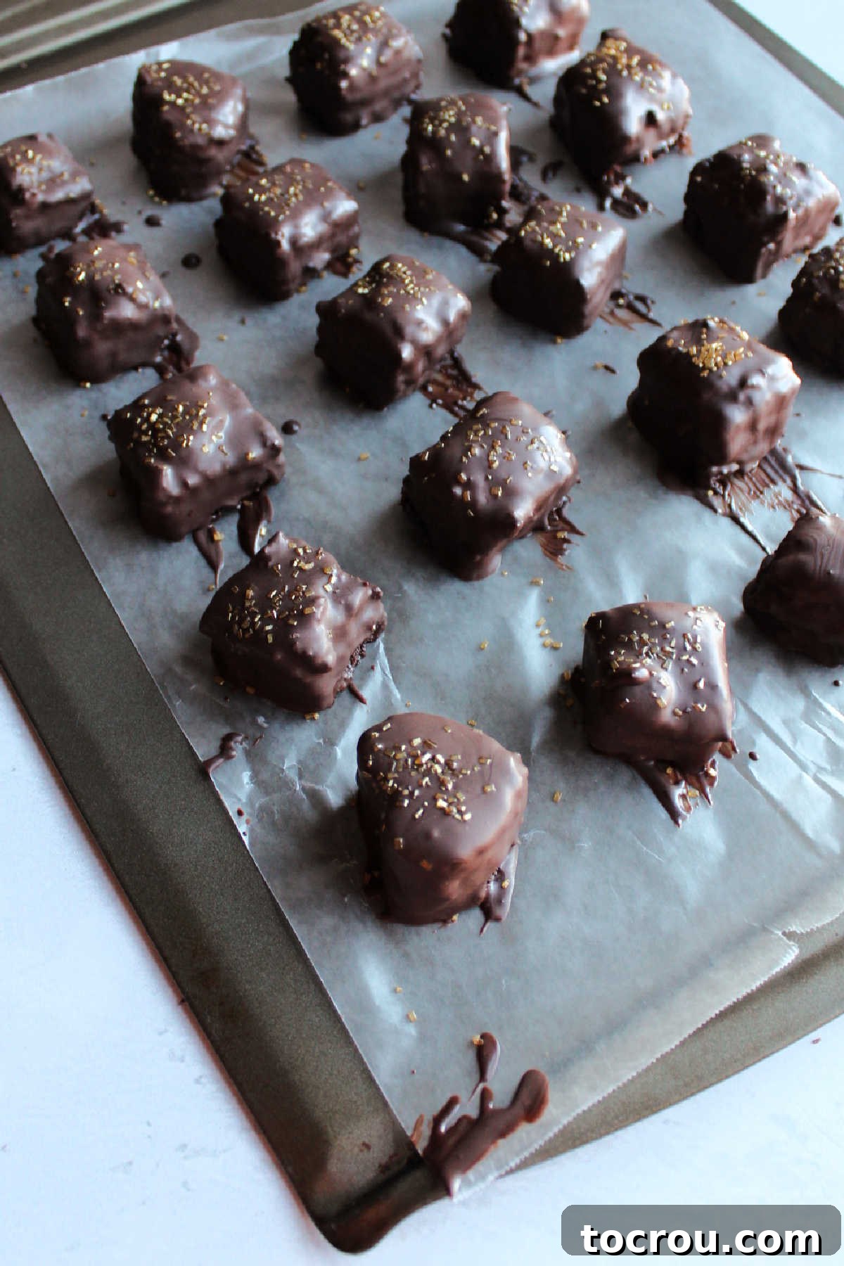 Freshly dipped chocolate petit fours, adorned with colorful sprinkles, meticulously arranged on wax paper to set and solidify.