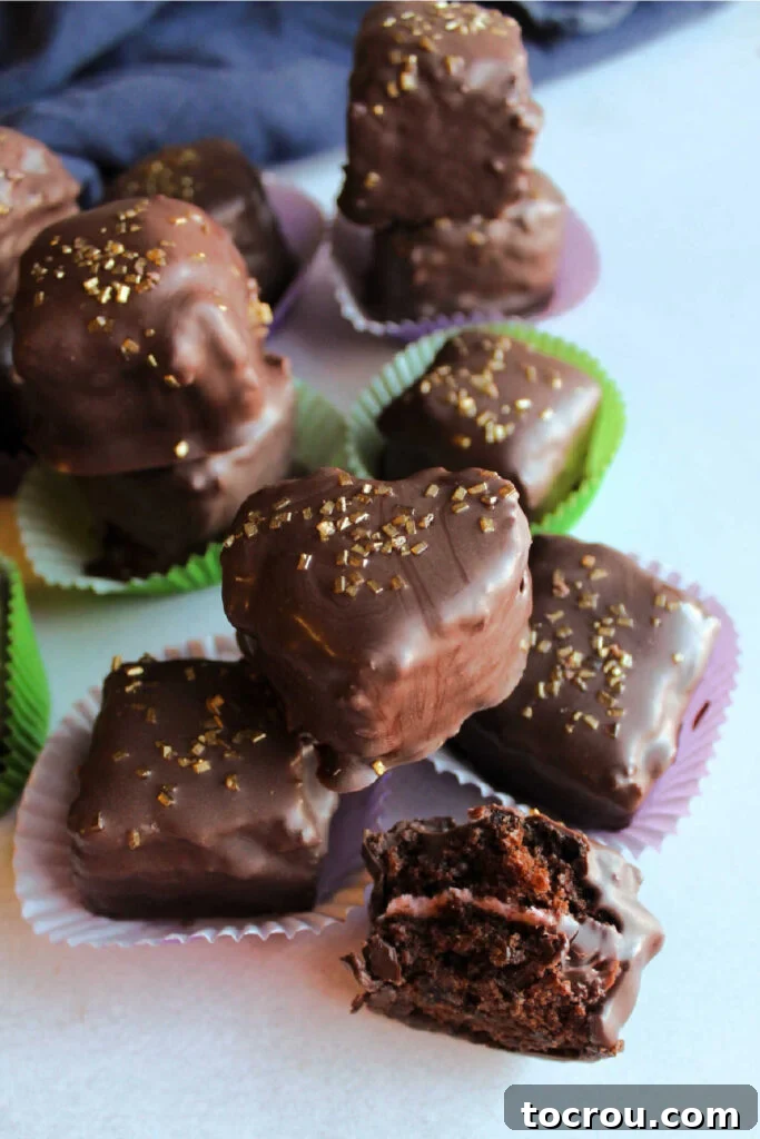 A charming stack of chocolate petit fours, with one expertly cut in half to showcase the exquisite layers of rich chocolate cake and creamy strawberry buttercream at its heart.