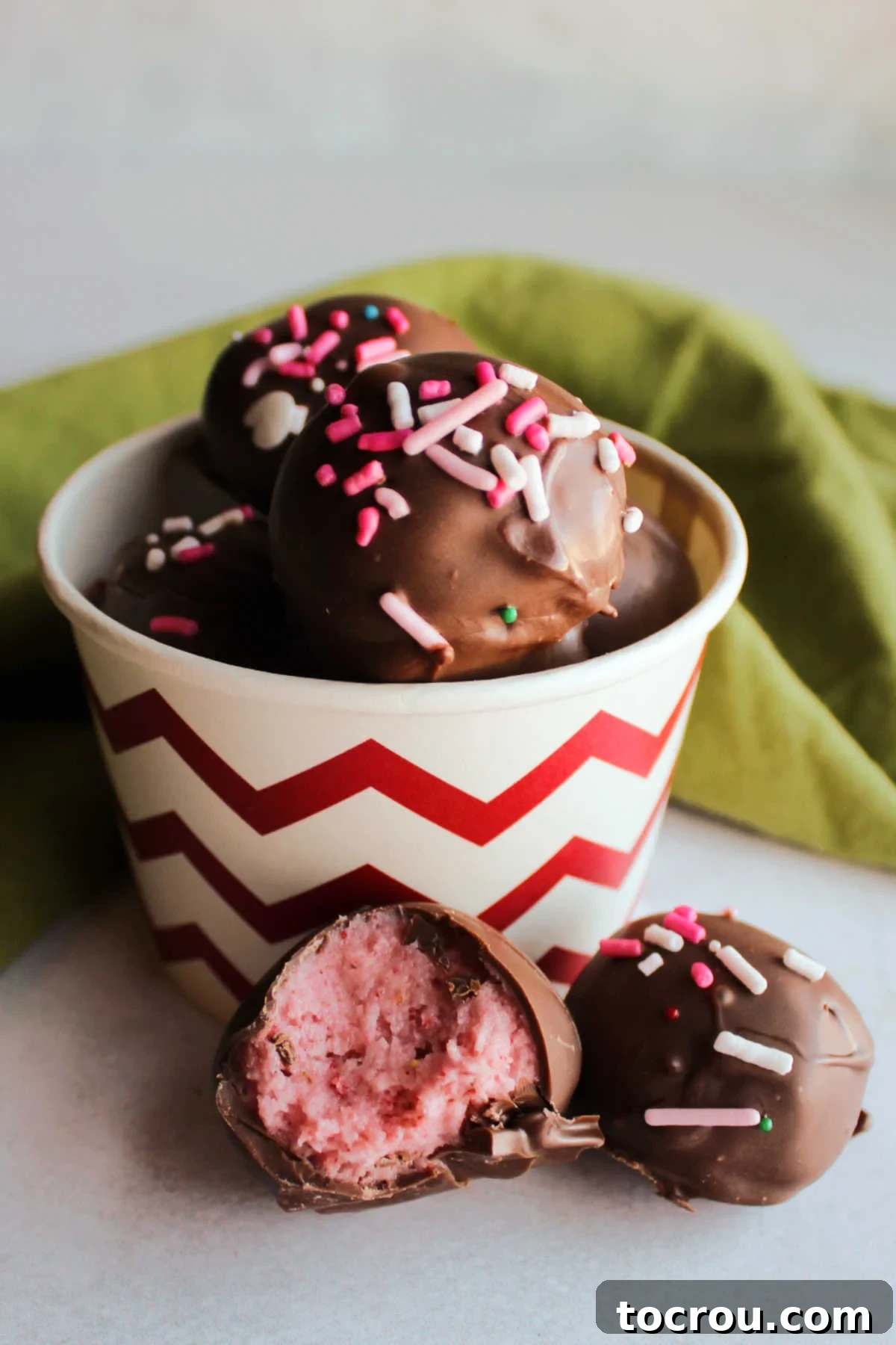 Decadent Strawberry Buttercream Truffles 6 A bowl filled with strawberry buttercream truffles, with one partially eaten, revealing its vibrant pink, soft interior.