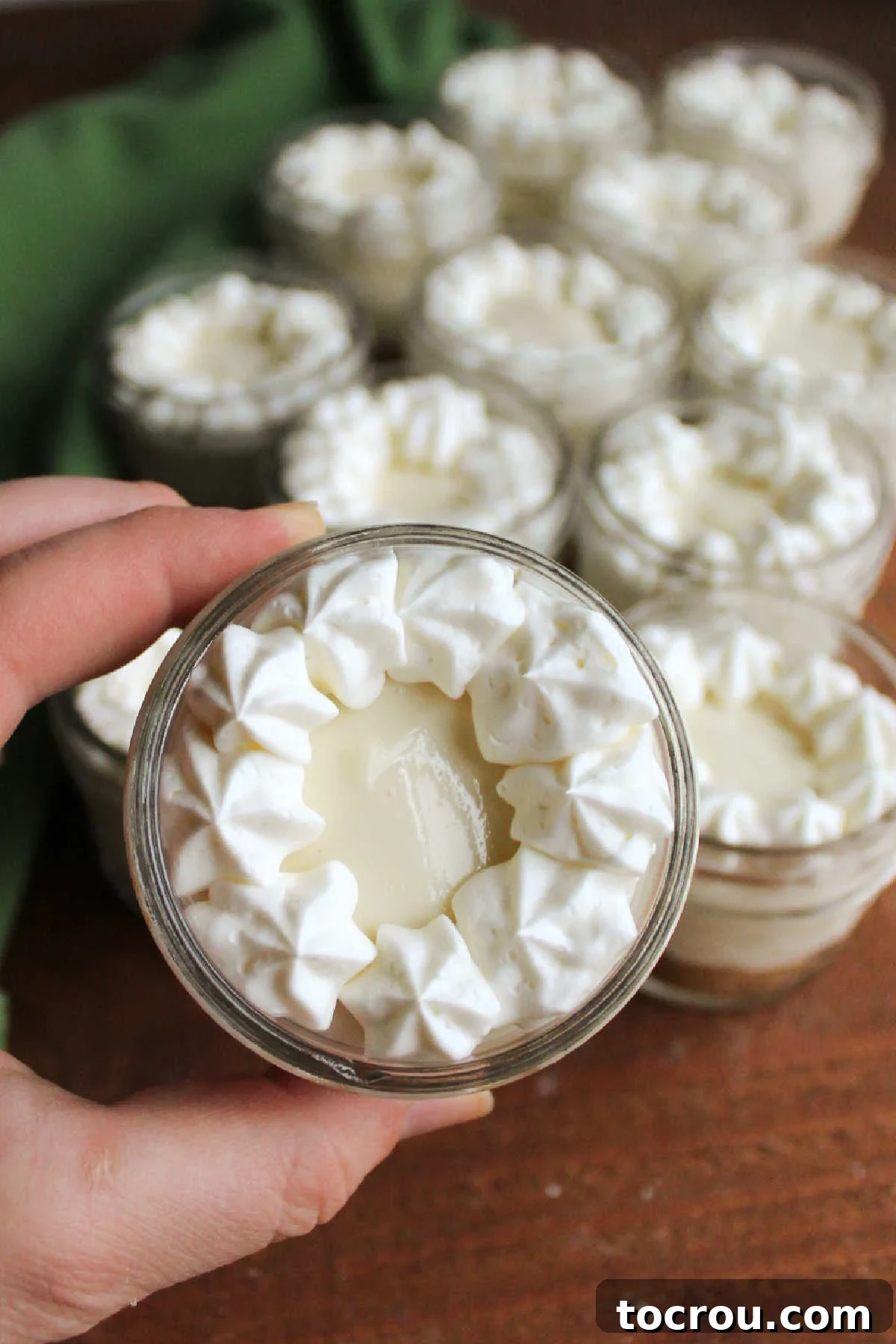Zesty Key Lime Cheesecake Jars 3 Hand holding a finished jar of no-bake key lime cheesecake, adorned with a decorative cream cheese whipped cream border, ready to be enjoyed.