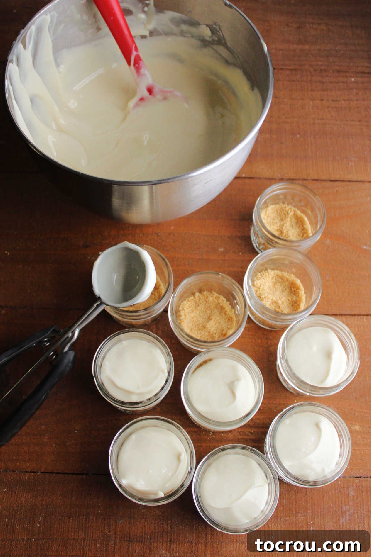 Zesty Key Lime Cheesecake Jars 4 Smooth key lime cheesecake mixture being carefully scooped over a graham cracker crust into small glass jars.
