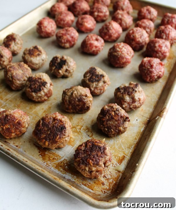 A sheet pan showcasing a mixture of beautifully browned and raw porcupine meatballs, ready for their flavorful sauce, highlighting the preparation process before simmering.