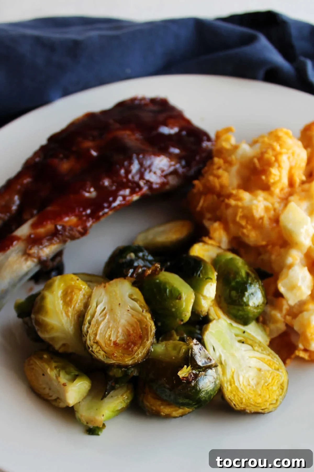 Close up of roasted brussels sprouts on plate with cheesy potatoes and BBQ ribs.