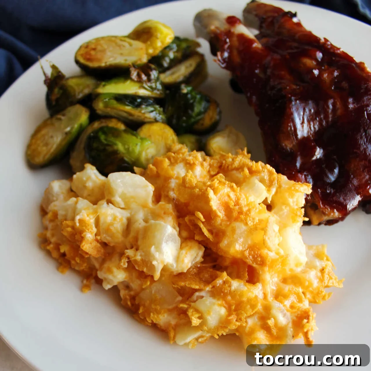 Cheddar Ranch Cheesy Potato Casserole Served Close up of cheesy ranch potatoes on dinner plate with brussels sprouts and bbq ribs.
