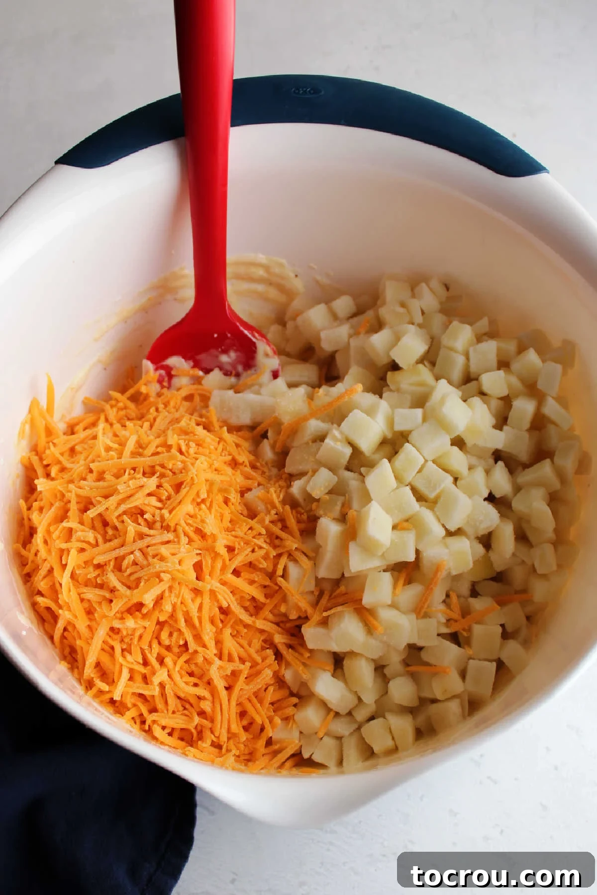 Potatoes and Cheese Ready for Mixing Shredded cheddar and cubes of potato in bowl with ranch mixture.