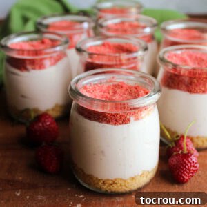 Jars of no bake cheesecake with a vanilla cookie crumb crust, creamy strawberry cheesecake filling, and a topping of freeze-dried strawberry and cookie crumbs.