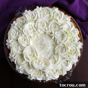 A whole key lime pie, beautifully adorned with piped whipped cream rosettes and delicate edible flowers on top, ready for serving.