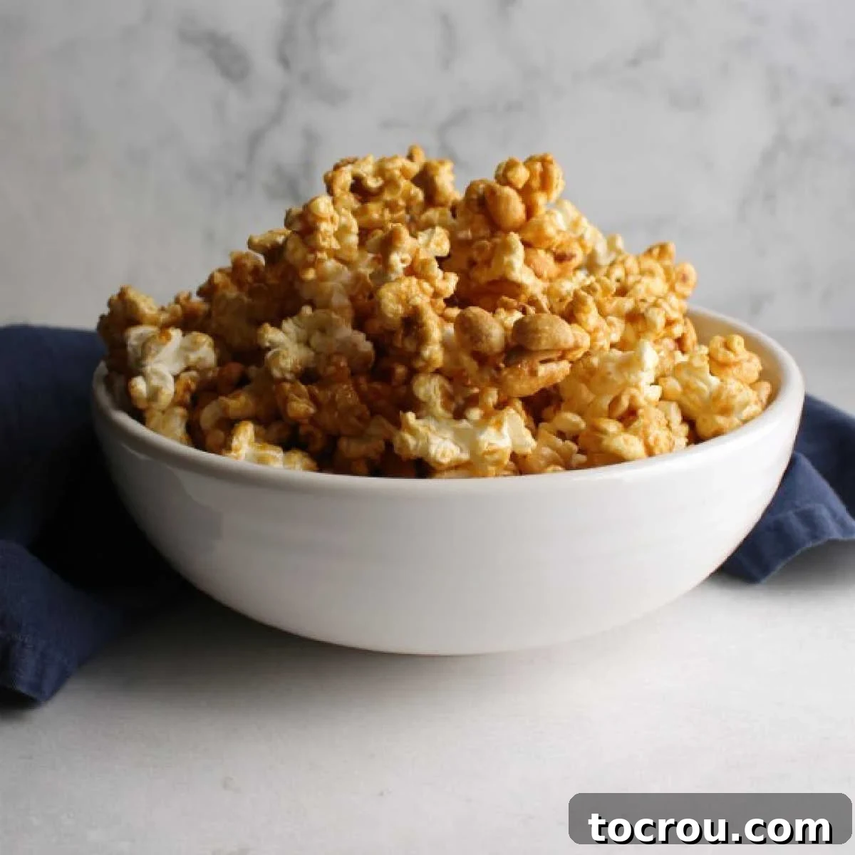White bowl filled with cracker jack style crunchy caramel corn, generously mixed with peanuts.