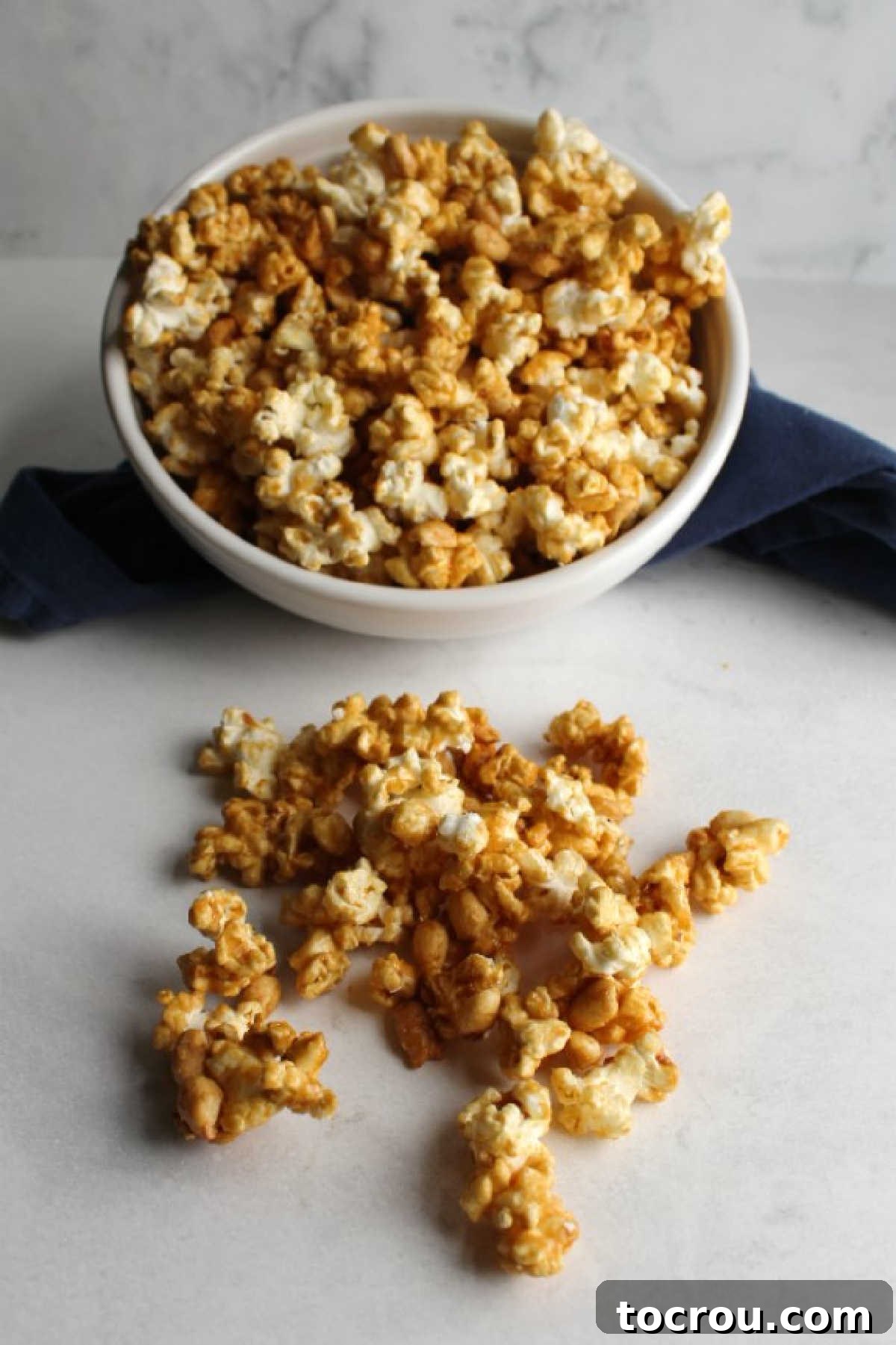 A bowl of crunchy caramel popcorn and peanuts, with some pieces artfully spilling onto the counter, highlighting its appealing texture.