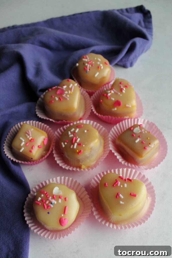 Petit fours coated with white icing and topped with pink and white sprinkles.
