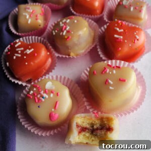 Petit fours in paper wrappers with one missing a bite showing raspberry filling.