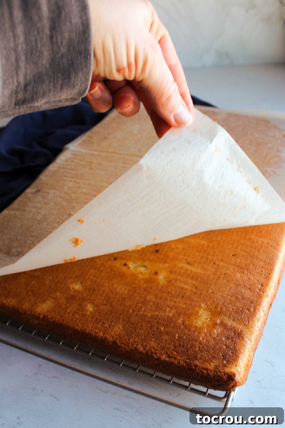 Peeling parchment paper off the bottom of the sheet of vanilla cake. 