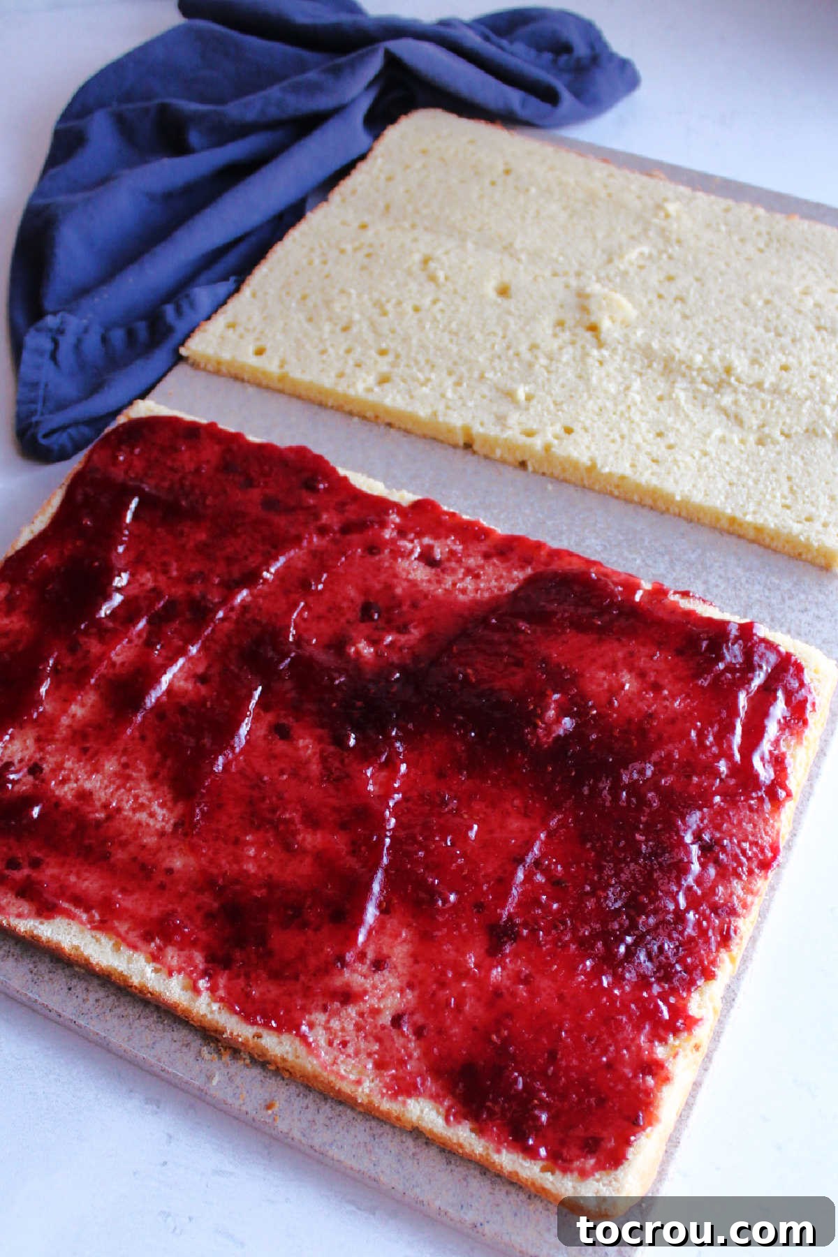 Torted cake halves with raspberry jam spread over the bottom half with the top half nearby ready to go back on top.
