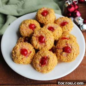 A beautifully arranged platter of cherry winks cookies, featuring a delicate pink cookie peeking through a crunchy cornflake crumb exterior, highlighted by a vibrant red maraschino cherry in the center.