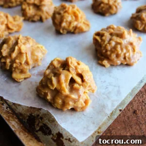 Delightful mounds of peanut butter honey cornflake cookies, arranged on a wax paper-lined pan, showcasing their inviting texture and ready to be enjoyed.