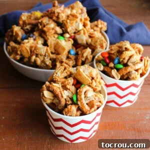 Two charming small cups overflowing with crunchy peanut butter Chex mix, featuring a delicious blend of cereal, pretzels, peanuts, and chocolate candies, all coated in a sweet and savory caramel.