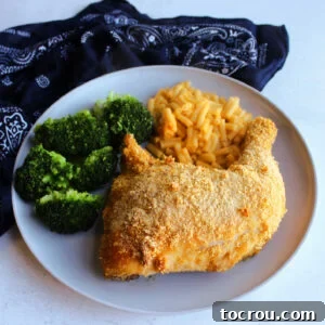 A satisfying dinner plate featuring a crispy cornflake crumb-coated chicken leg quarter, served alongside creamy mac and cheese and vibrant steamed broccoli.