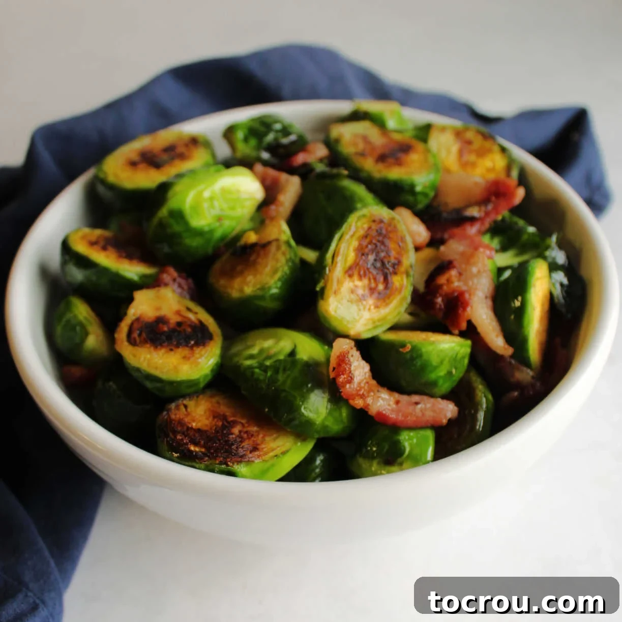 Serving bowl filled with golden brown Brussels sprouts halves and bits of bacon, fresh from the stove.